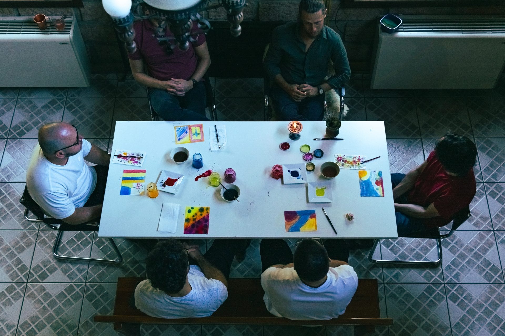 Vista de cima da mesa branca, com os homens pintando em aquarela.