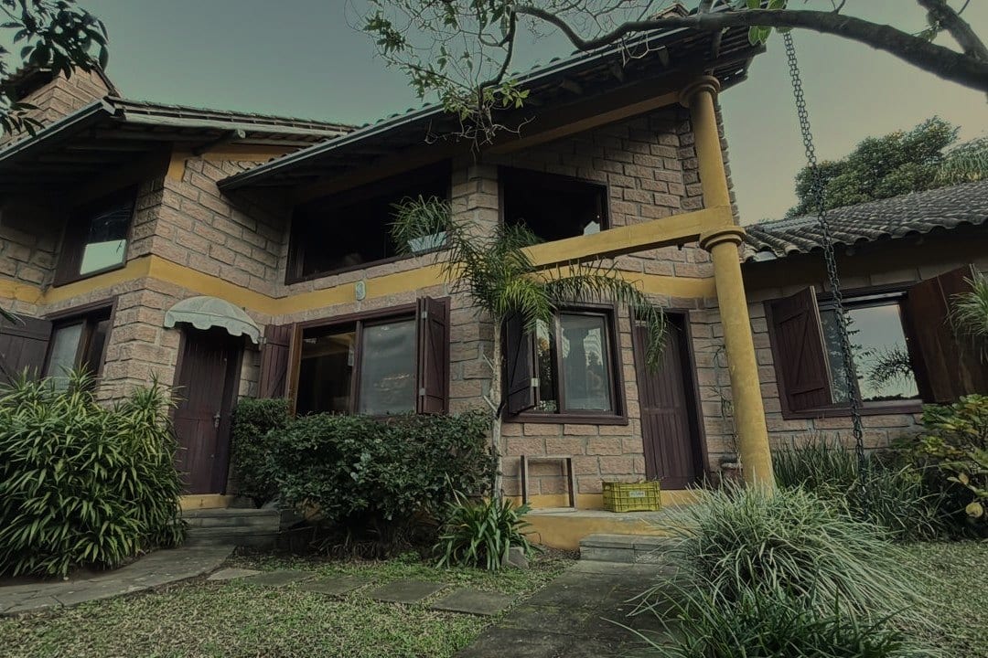 A casa de pedra por fora, com as varandas de madeira amarela e o jardim em volta.
