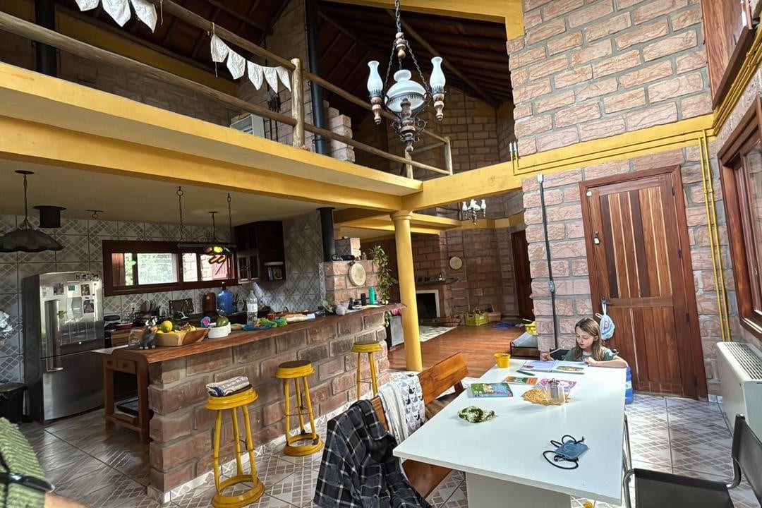A cozinha aberta, com o balcão, a mesa grande e o mezanino de madeira.