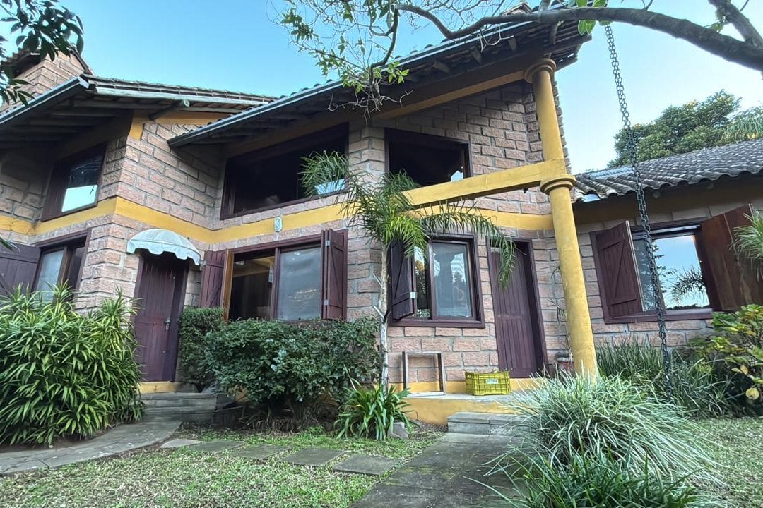 A casa por fora, de pedra e madeira, com a varanda e o jardim em volta.