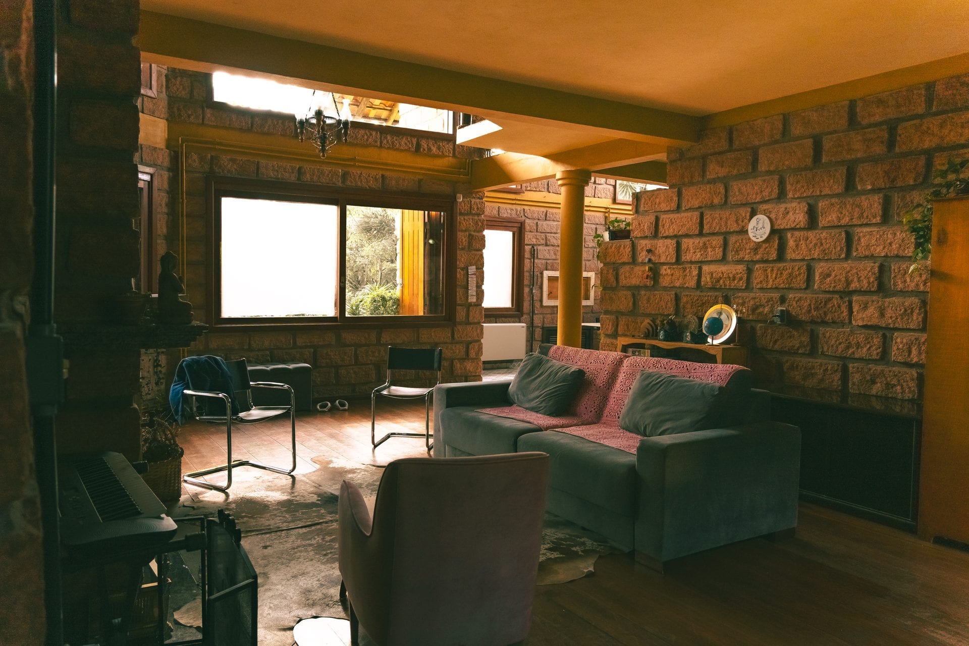 O salão principal da casa, de tijolo e madeira, com o sofá e a luz da tarde entrando pelas janelas.