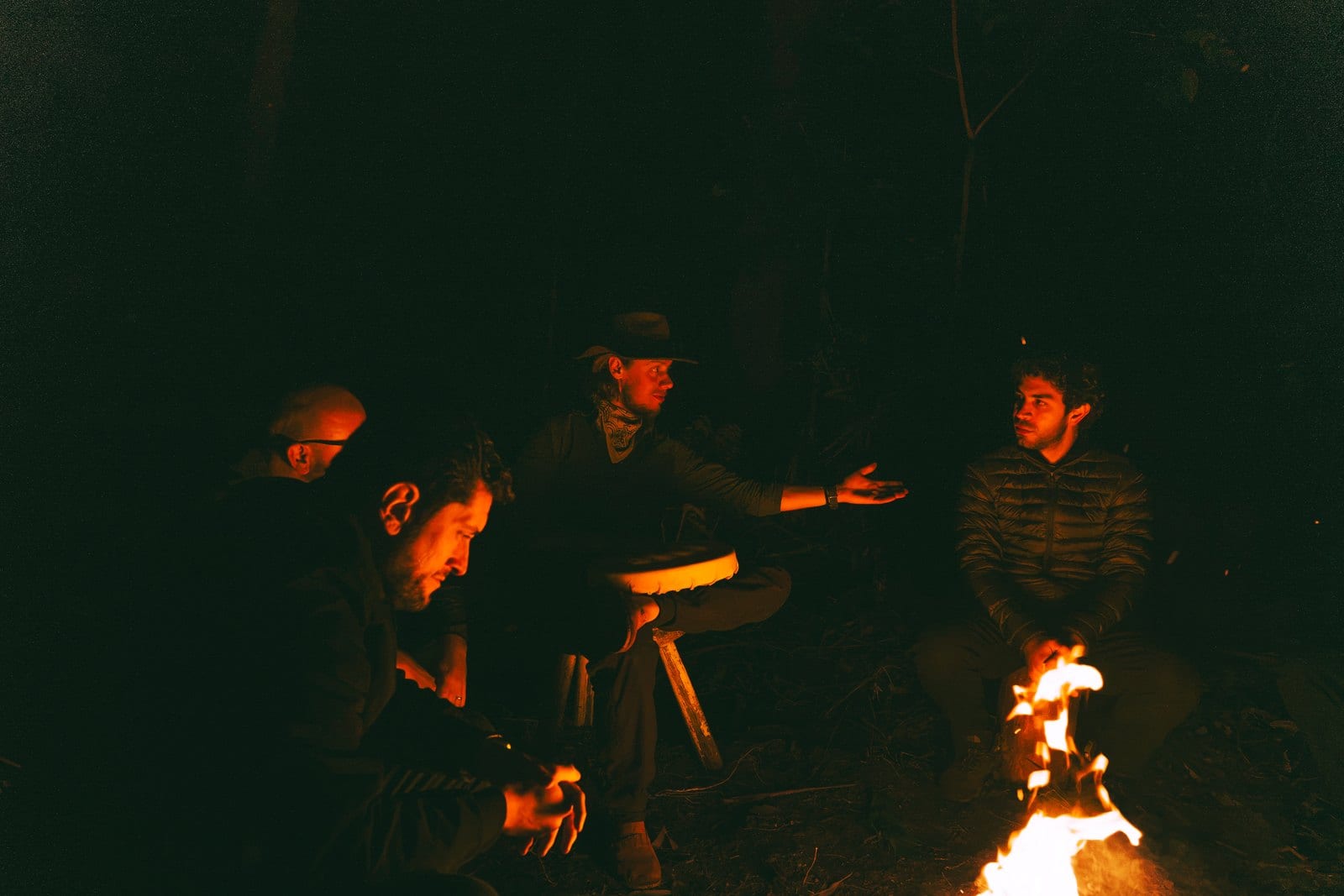Os homens sentados em roda em volta da fogueira, no escuro do mato.