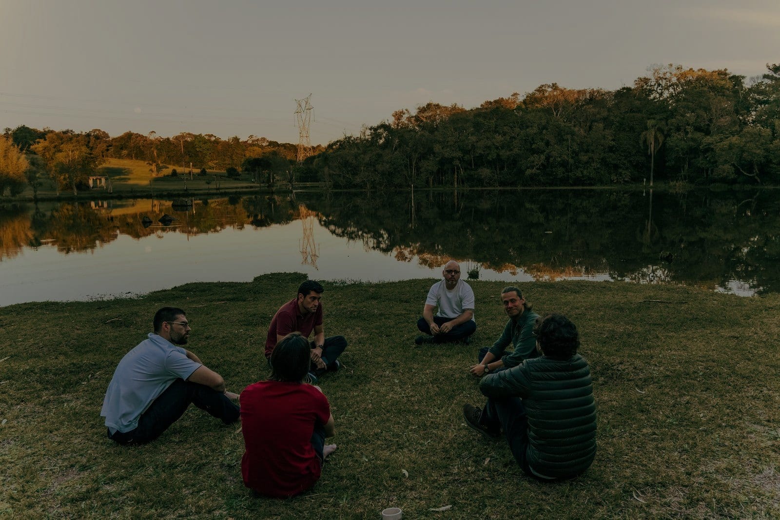A turma sentada em roda na grama à beira do lago, no fim da tarde.